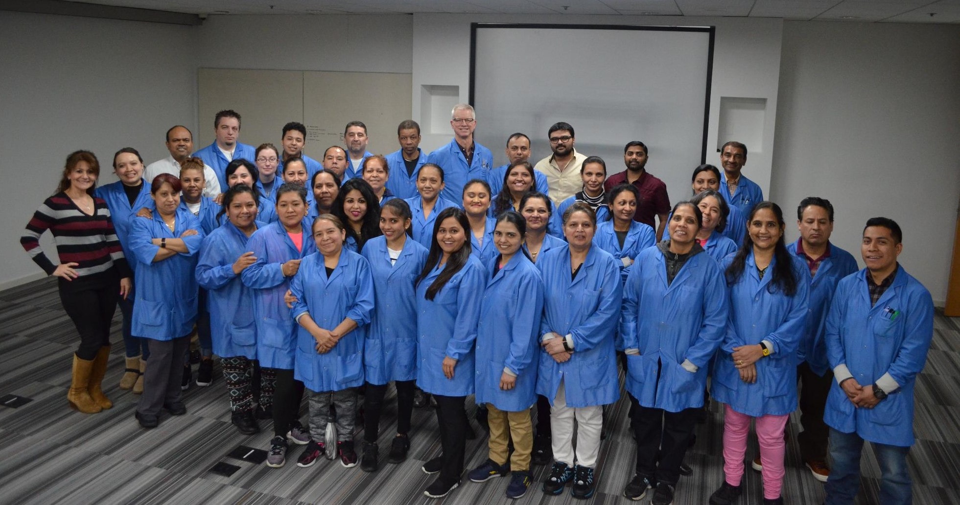 Group of people in blue lab coats posing for a photo in an indoor setting